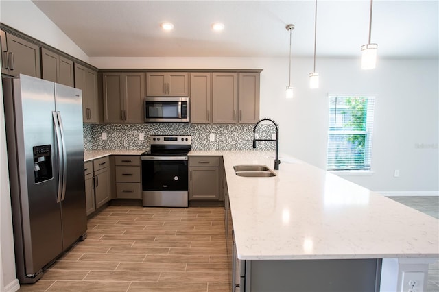 kitchen featuring light stone countertops, sink, stainless steel appliances, pendant lighting, and vaulted ceiling