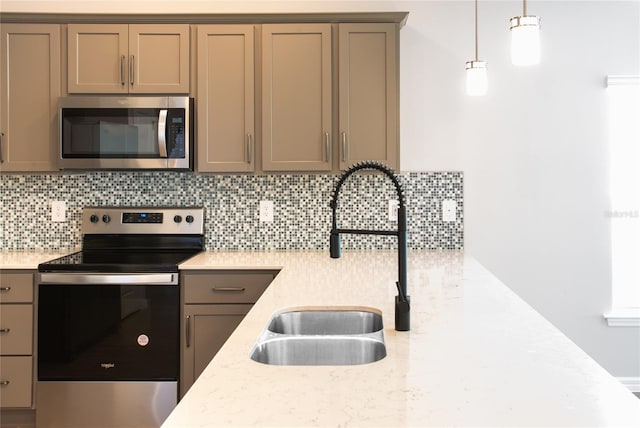 kitchen featuring decorative backsplash, appliances with stainless steel finishes, light stone counters, sink, and hanging light fixtures