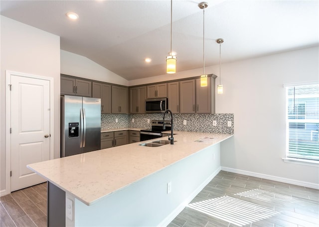 kitchen with sink, hanging light fixtures, kitchen peninsula, vaulted ceiling, and appliances with stainless steel finishes