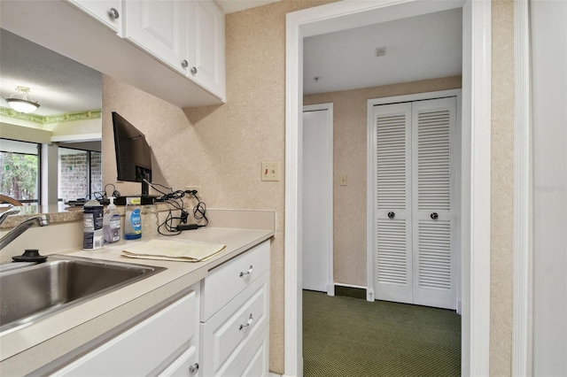 kitchen featuring carpet flooring, white cabinetry, and sink