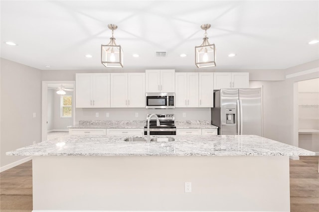 kitchen with white cabinets, hanging light fixtures, a kitchen island with sink, and appliances with stainless steel finishes