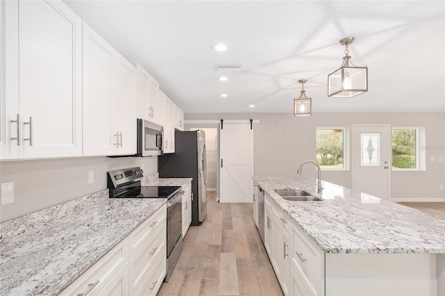 kitchen with sink, stainless steel appliances, a barn door, a kitchen island with sink, and white cabinets