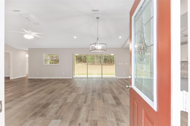 interior space with vaulted ceiling, ceiling fan with notable chandelier, and light wood-type flooring