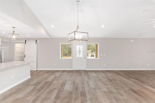 unfurnished living room with a barn door, vaulted ceiling, and light hardwood / wood-style flooring