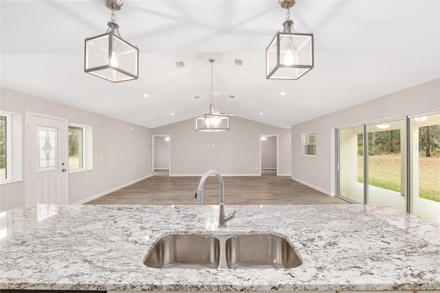 kitchen with pendant lighting, light stone counters, sink, and a wealth of natural light