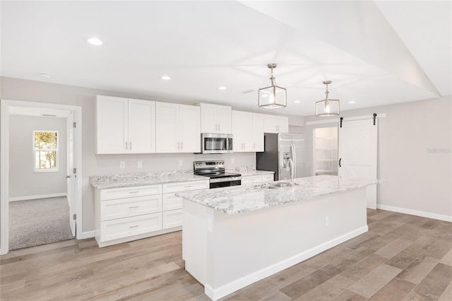 kitchen featuring appliances with stainless steel finishes, pendant lighting, a barn door, white cabinets, and an island with sink