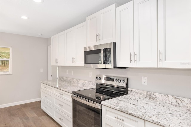 kitchen with white cabinets, light stone counters, stainless steel appliances, and light hardwood / wood-style flooring