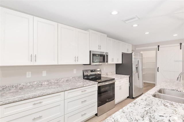 kitchen featuring light stone counters, stainless steel appliances, sink, a barn door, and white cabinetry