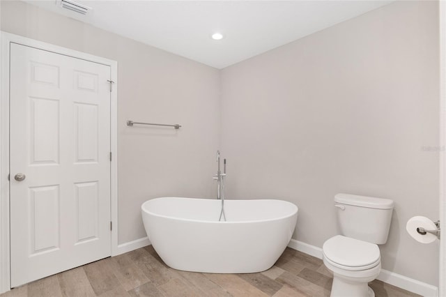 bathroom with a washtub, hardwood / wood-style floors, and toilet