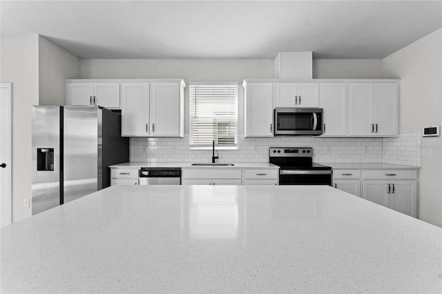 kitchen featuring decorative backsplash, appliances with stainless steel finishes, light stone countertops, sink, and white cabinets