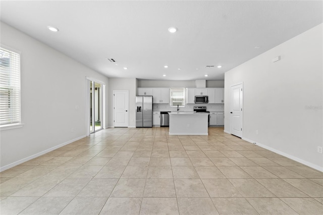 kitchen with white cabinetry, stainless steel appliances, light tile patterned floors, backsplash, and a kitchen island