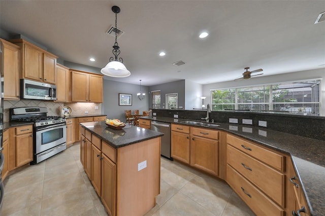 kitchen featuring ceiling fan with notable chandelier, sink, appliances with stainless steel finishes, decorative light fixtures, and a kitchen island