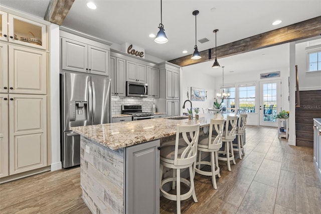 kitchen with beamed ceiling, light stone countertops, a kitchen island with sink, and appliances with stainless steel finishes