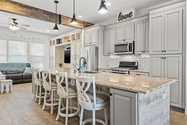 kitchen featuring beamed ceiling, decorative light fixtures, a kitchen bar, a center island with sink, and appliances with stainless steel finishes