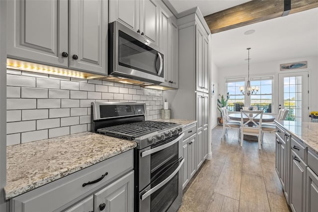 kitchen featuring appliances with stainless steel finishes, backsplash, an inviting chandelier, light hardwood / wood-style floors, and hanging light fixtures