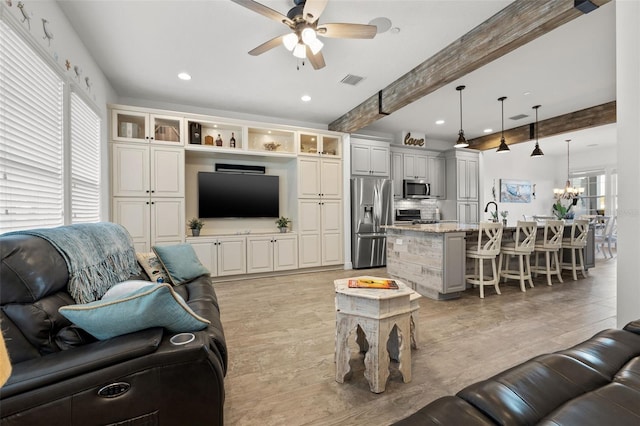 living room featuring beamed ceiling and ceiling fan with notable chandelier