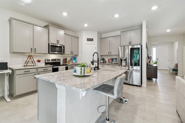 kitchen featuring appliances with stainless steel finishes, gray cabinetry, and an island with sink