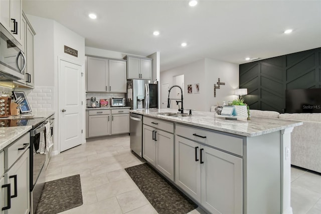 kitchen featuring sink, tasteful backsplash, gray cabinets, a center island with sink, and appliances with stainless steel finishes