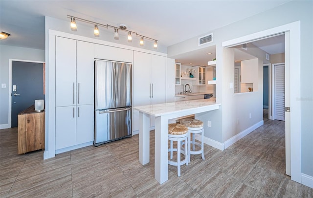 kitchen with stainless steel refrigerator, white cabinetry, sink, kitchen peninsula, and a breakfast bar