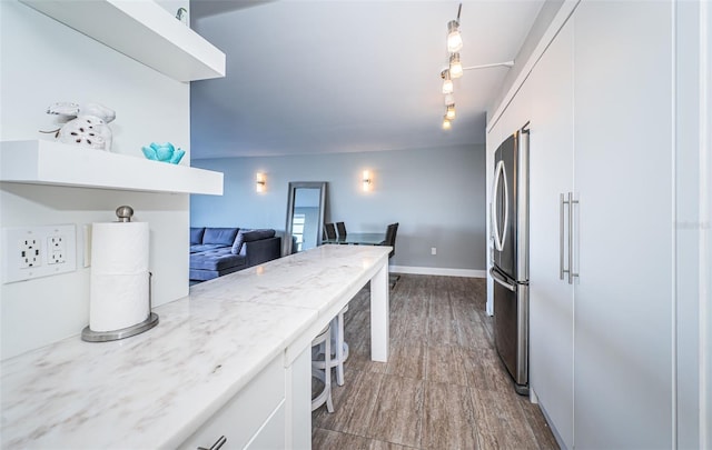 kitchen with a kitchen breakfast bar, hardwood / wood-style flooring, stainless steel fridge, decorative light fixtures, and white cabinetry