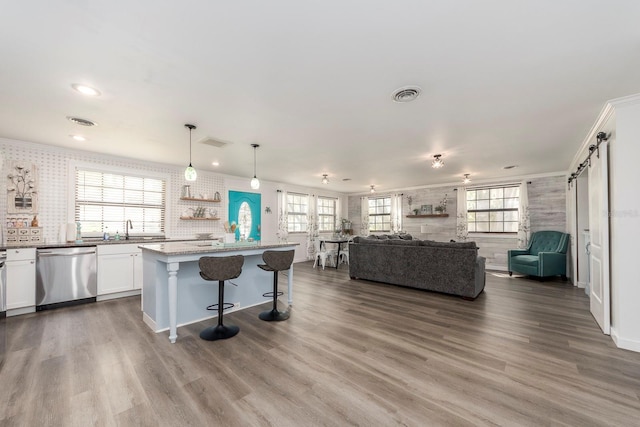 kitchen with stainless steel dishwasher, a healthy amount of sunlight, a barn door, decorative light fixtures, and white cabinetry