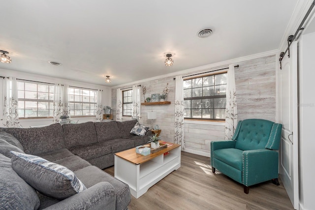 living room featuring wood-type flooring, a barn door, crown molding, and wood walls