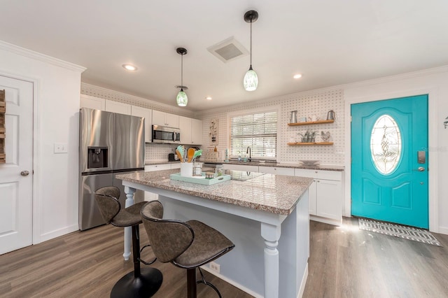 kitchen with dark wood-type flooring, stainless steel appliances, a kitchen island, decorative light fixtures, and white cabinets