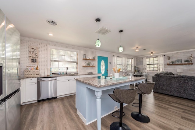 kitchen featuring light stone counters, stainless steel appliances, decorative light fixtures, a center island, and white cabinetry