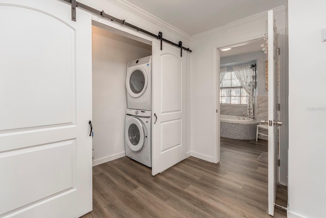 clothes washing area with a barn door, stacked washing maching and dryer, dark hardwood / wood-style floors, and crown molding