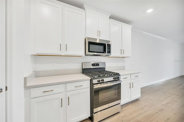 kitchen featuring light wood-type flooring, white cabinetry, stainless steel appliances, and ornamental molding