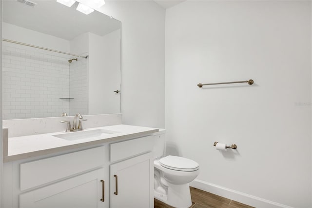 bathroom with hardwood / wood-style flooring, vanity, toilet, and tiled shower