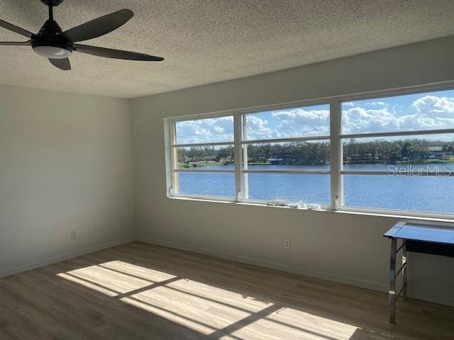 unfurnished room featuring wood-type flooring, a water view, and ceiling fan