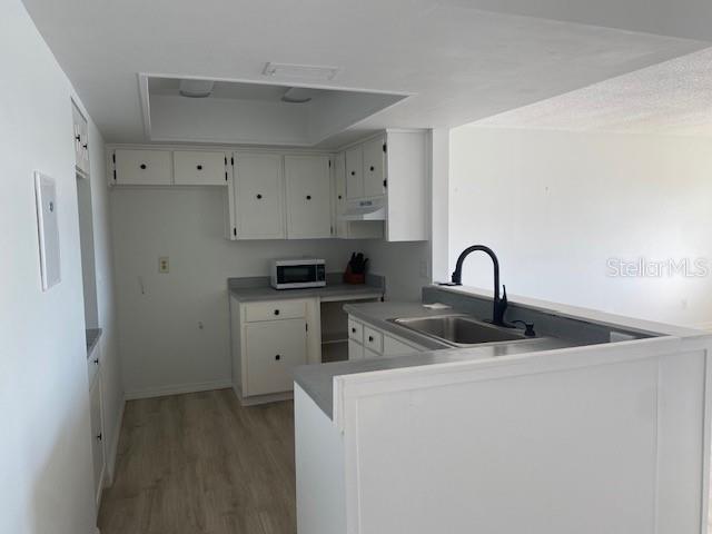 kitchen with white cabinets, light hardwood / wood-style floors, kitchen peninsula, and sink