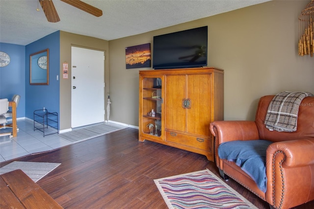 living area with ceiling fan, wood-type flooring, and a textured ceiling