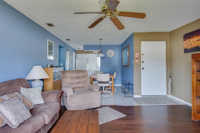 living room featuring ceiling fan, light hardwood / wood-style flooring, and a textured ceiling