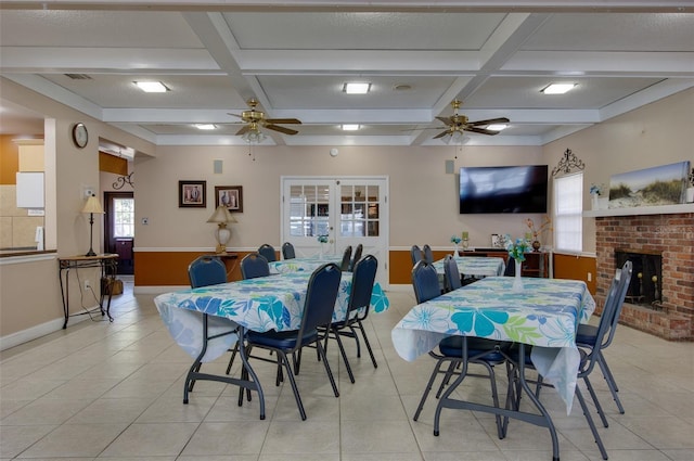 tiled dining area featuring ceiling fan, a fireplace, beamed ceiling, and coffered ceiling