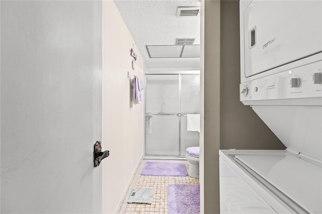 bathroom with tile patterned flooring, toilet, a textured ceiling, and stacked washer and clothes dryer