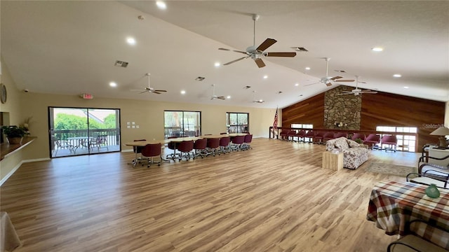 living room featuring high vaulted ceiling, ceiling fan, wooden walls, and light hardwood / wood-style flooring