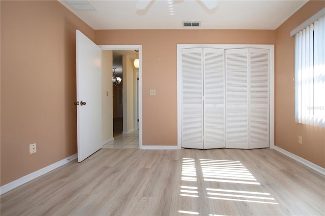 unfurnished bedroom featuring a closet, ceiling fan with notable chandelier, and light wood-type flooring