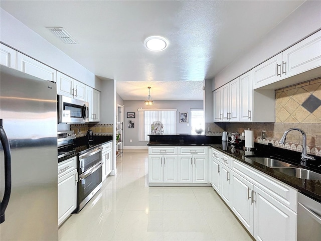 kitchen with backsplash, hanging light fixtures, sink, appliances with stainless steel finishes, and white cabinetry