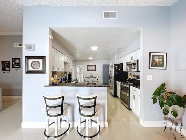 kitchen featuring kitchen peninsula, appliances with stainless steel finishes, a textured ceiling, and white cabinetry