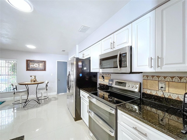 kitchen with appliances with stainless steel finishes, white cabinetry, dark stone counters, and light tile patterned flooring