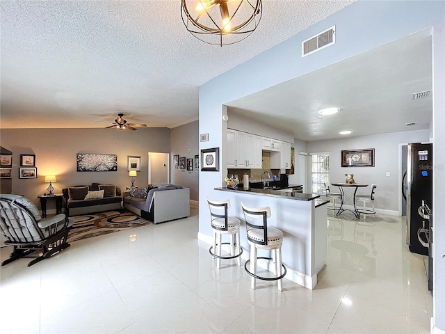 kitchen featuring kitchen peninsula, stainless steel fridge, a textured ceiling, white cabinetry, and a breakfast bar area