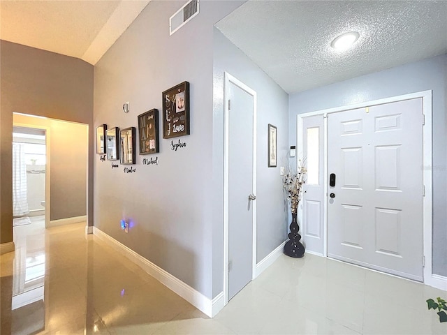 foyer entrance with light tile patterned floors, a textured ceiling, and lofted ceiling