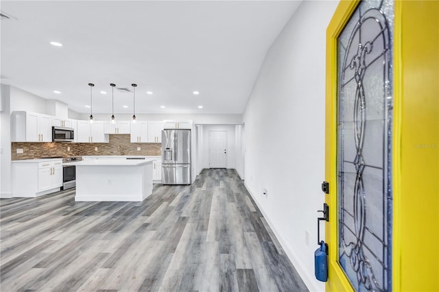 kitchen with pendant lighting, light wood-type flooring, appliances with stainless steel finishes, a kitchen island, and white cabinetry