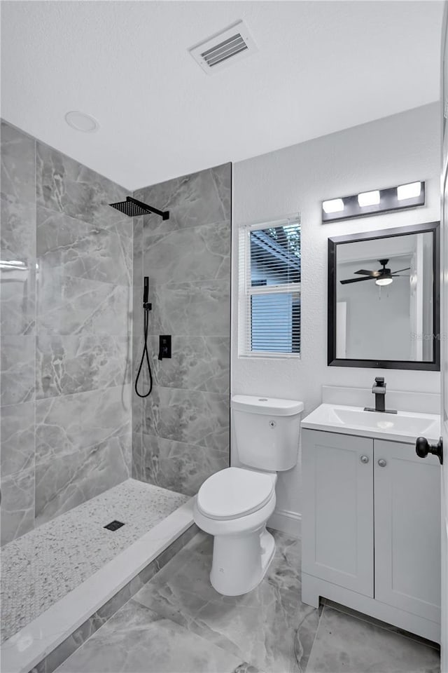 bathroom featuring tiled shower, ceiling fan, vanity, and toilet