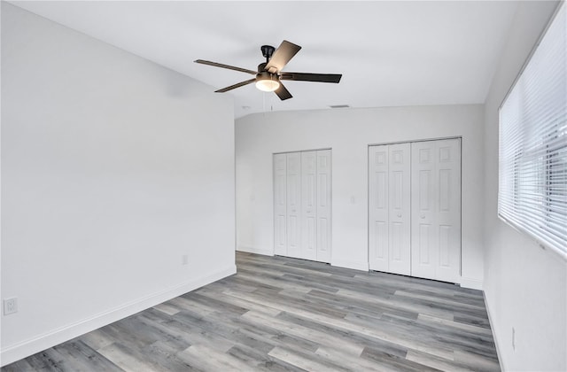 unfurnished bedroom featuring two closets, ceiling fan, light hardwood / wood-style flooring, and vaulted ceiling