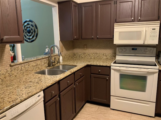 kitchen featuring sink, dark brown cabinets, white appliances, light stone countertops, and backsplash