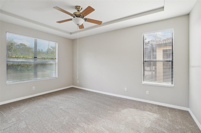 spare room featuring ceiling fan, carpet floors, a tray ceiling, and baseboards