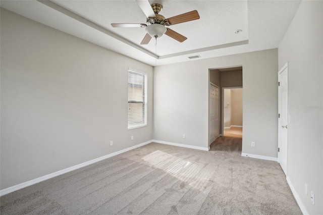 spare room with ceiling fan, a raised ceiling, and light carpet